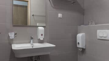 A modern bathroom with a white sink, mirror, and toilet. There are towel racks and a soap dispenser on the wall.