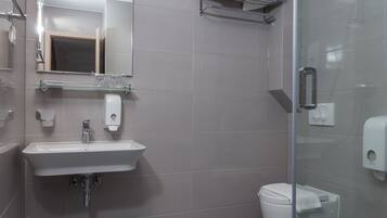 Un baño moderno con cabina de ducha de vidrio, un lavabo blanco y un inodoro.