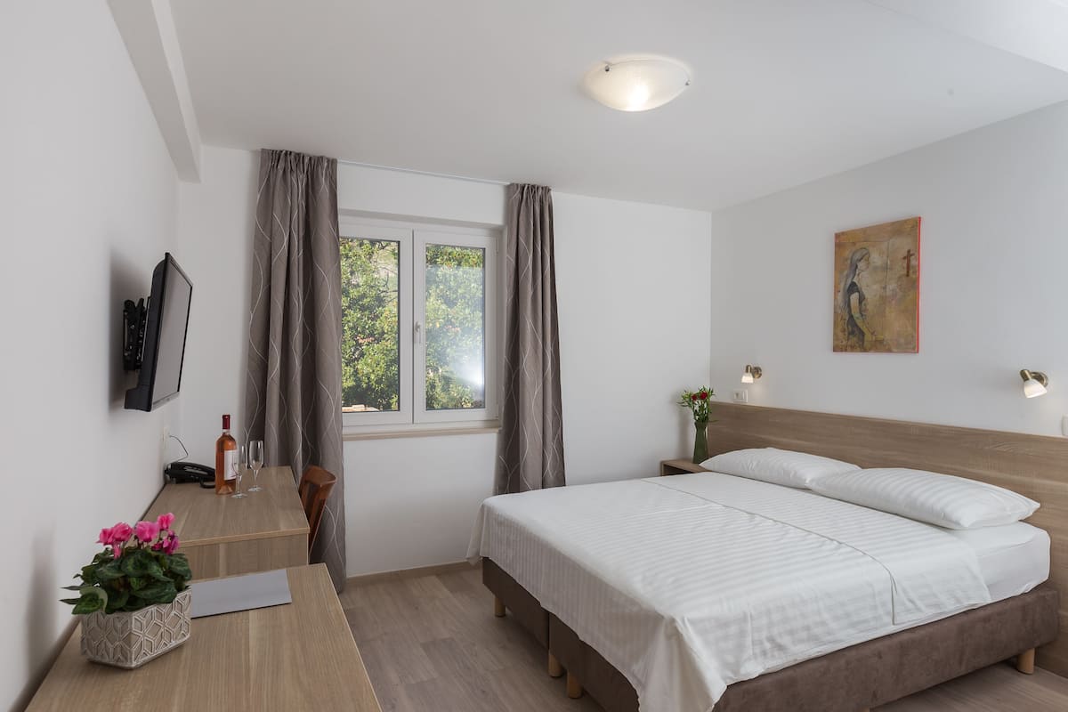 A modern bedroom with a bed, bedside tables, a TV, and a window with curtains.