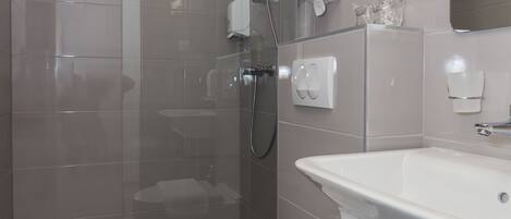Un baño moderno con ducha envuelta en vidrio, un inodoro blanco y un lavamanos con espejo arriba.