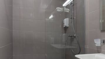 A modern shower area with a glass door, a handheld showerhead, and a wall-mounted soap dispenser.