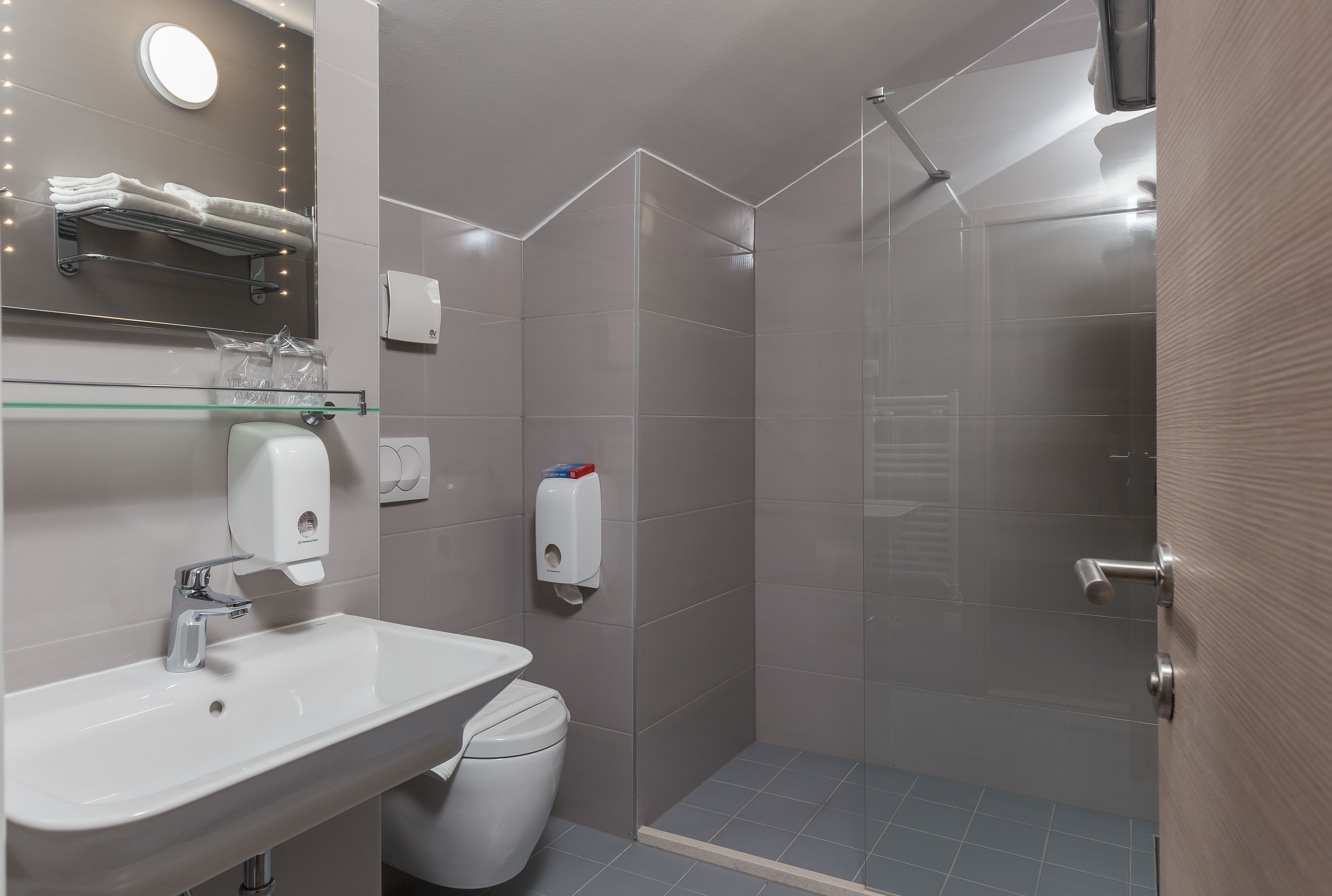 Un baño moderno con cabina de ducha de vidrio, un lavamanos blanco y un estante de vidrio sobre el espejo.