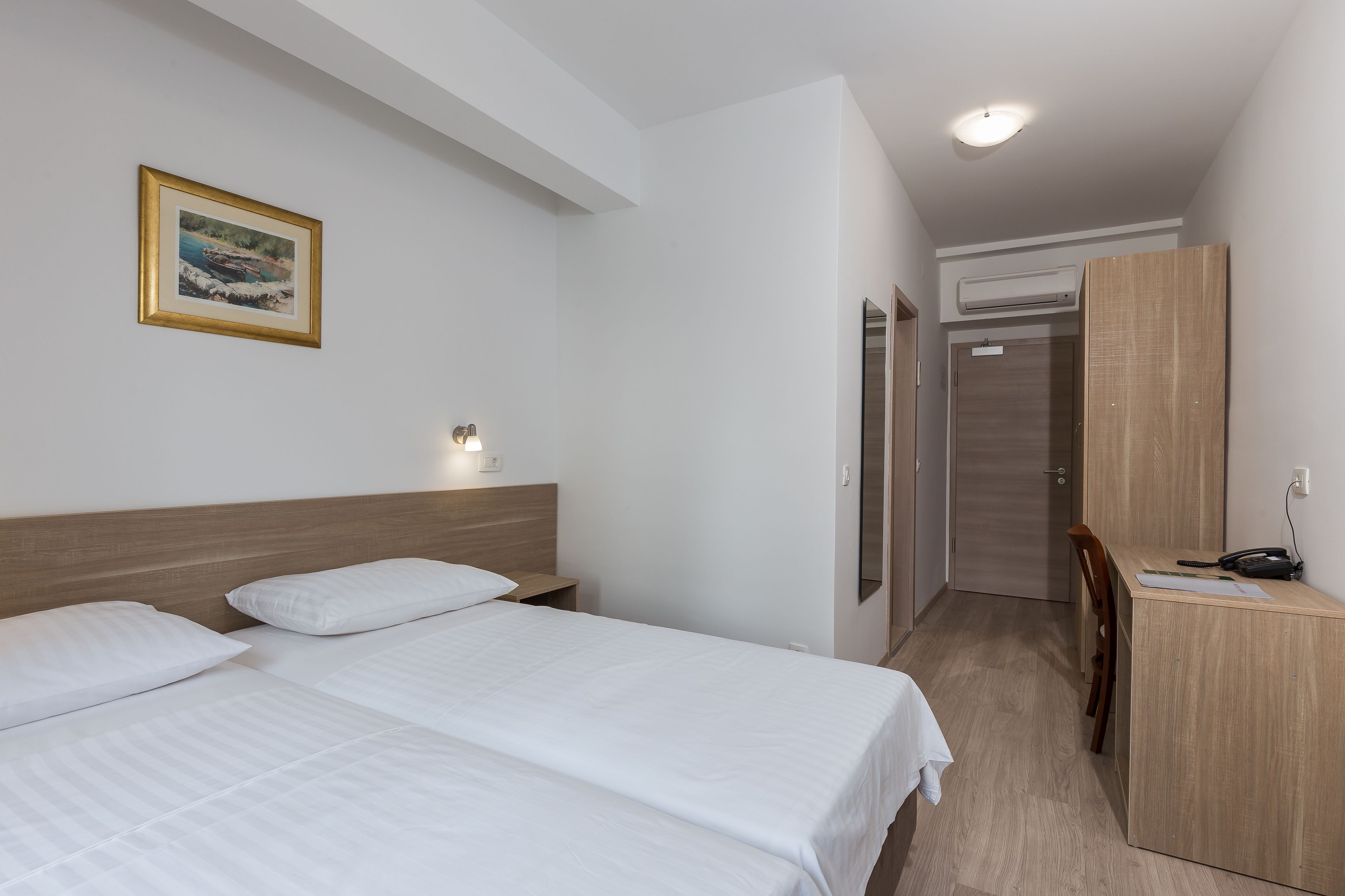 A hotel room with two beds, a desk, a chair, a wardrobe, and a framed picture on the wall.