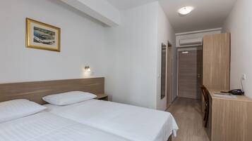 Habitación de hotel con dos camas, un escritorio, una silla, un armario y un cuadro en la pared.