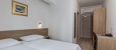 Quarto de hotel com duas camas, uma escrivaninha, uma cadeira, um guarda-roupa e um quadro na parede.