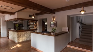 Zona de recepción con mostrador de piedra, bar con estantes llenos de botellas y una escalera.