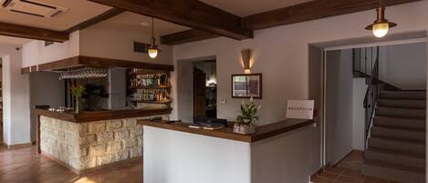 A reception area with a stone counter, a bar with shelves of bottles, and a staircase.