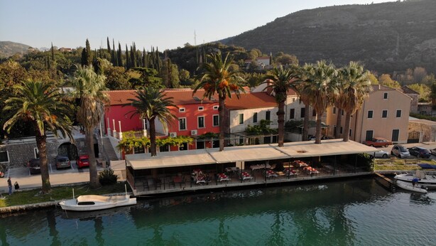 Un restaurante frente al mar con terraza, un barco amarrado cerca y edificios al fondo.