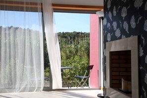 Um quarto com uma janela grande, lareira e vista para o verde lá fora.