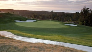 A golf course with sand bunkers, a water hazard, and a view of the ocean.