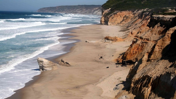 A coastal beach with a sandy shore, cliffs, and ocean waves.