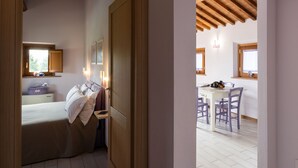 Ein Schlafzimmer mit Bett, Nachttisch und Fenster. Das Zimmer verfügt über Holzbalken an der Decke und eine weiße Wand.