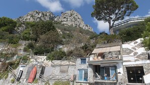 Een gebouw aan de kust met een gevel van natuursteen, een balkon met uitzicht op zee en een berg op de achtergrond.