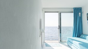 Een balkon met uitzicht op zee, een blauwe bank en een deur naar buiten.