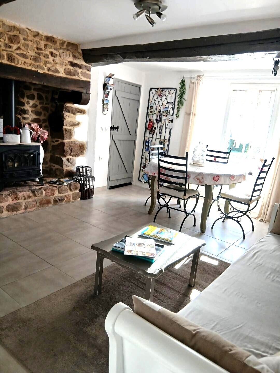 A cozy living room with a stone fireplace, a dining area with a table and chairs, and a large window allowing natural light.