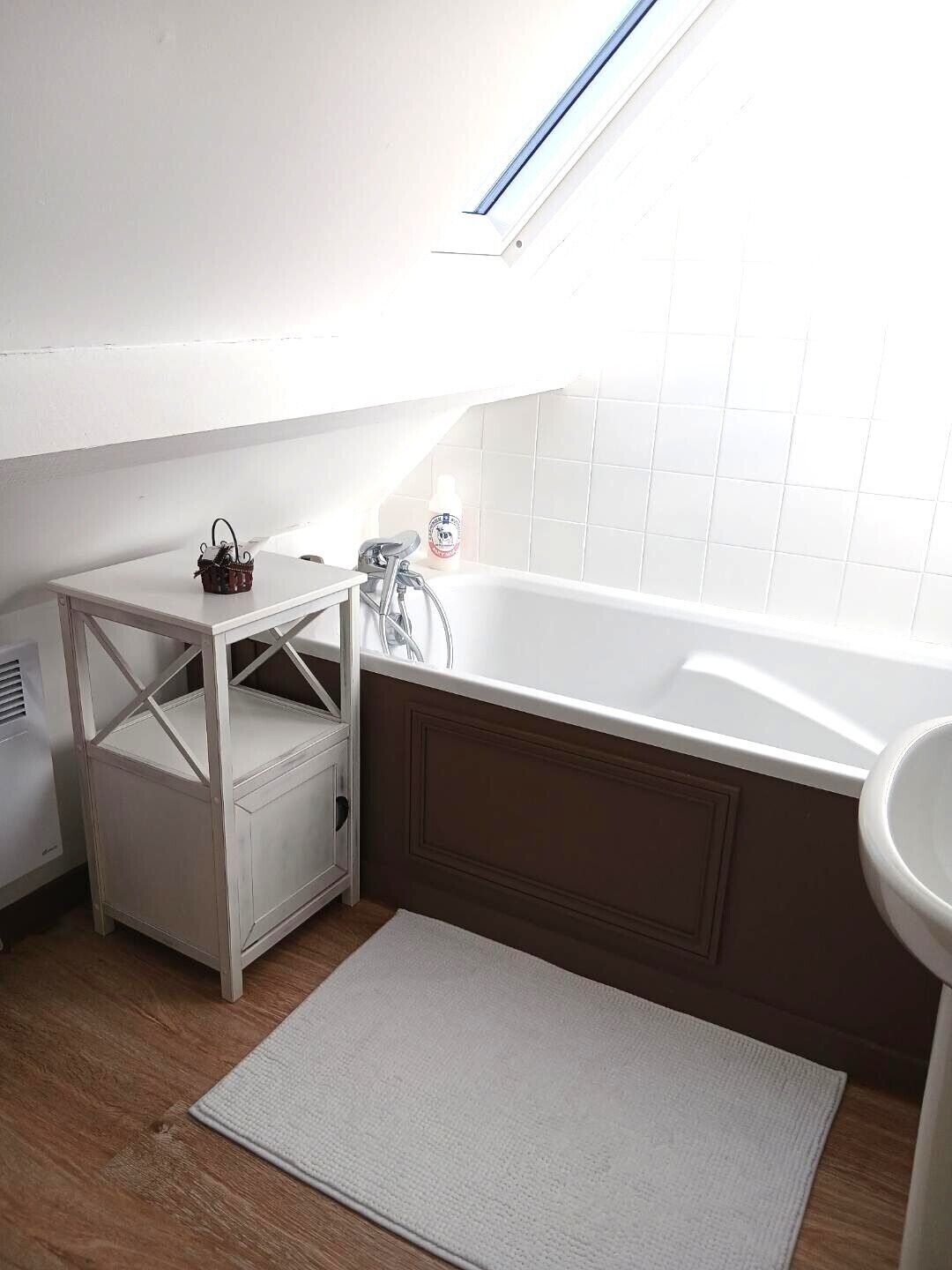 Un baño pequeño y moderno con una bañera blanca, un tocador blanco y una pequeña mesa con una botella de jabón de manos.