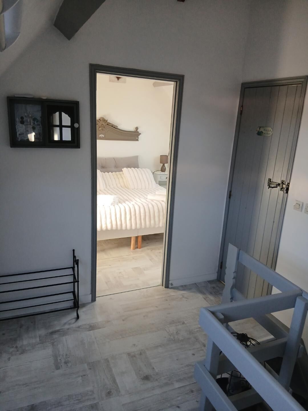 A bedroom with a bed, a nightstand, a dresser, and a door leading to another room.