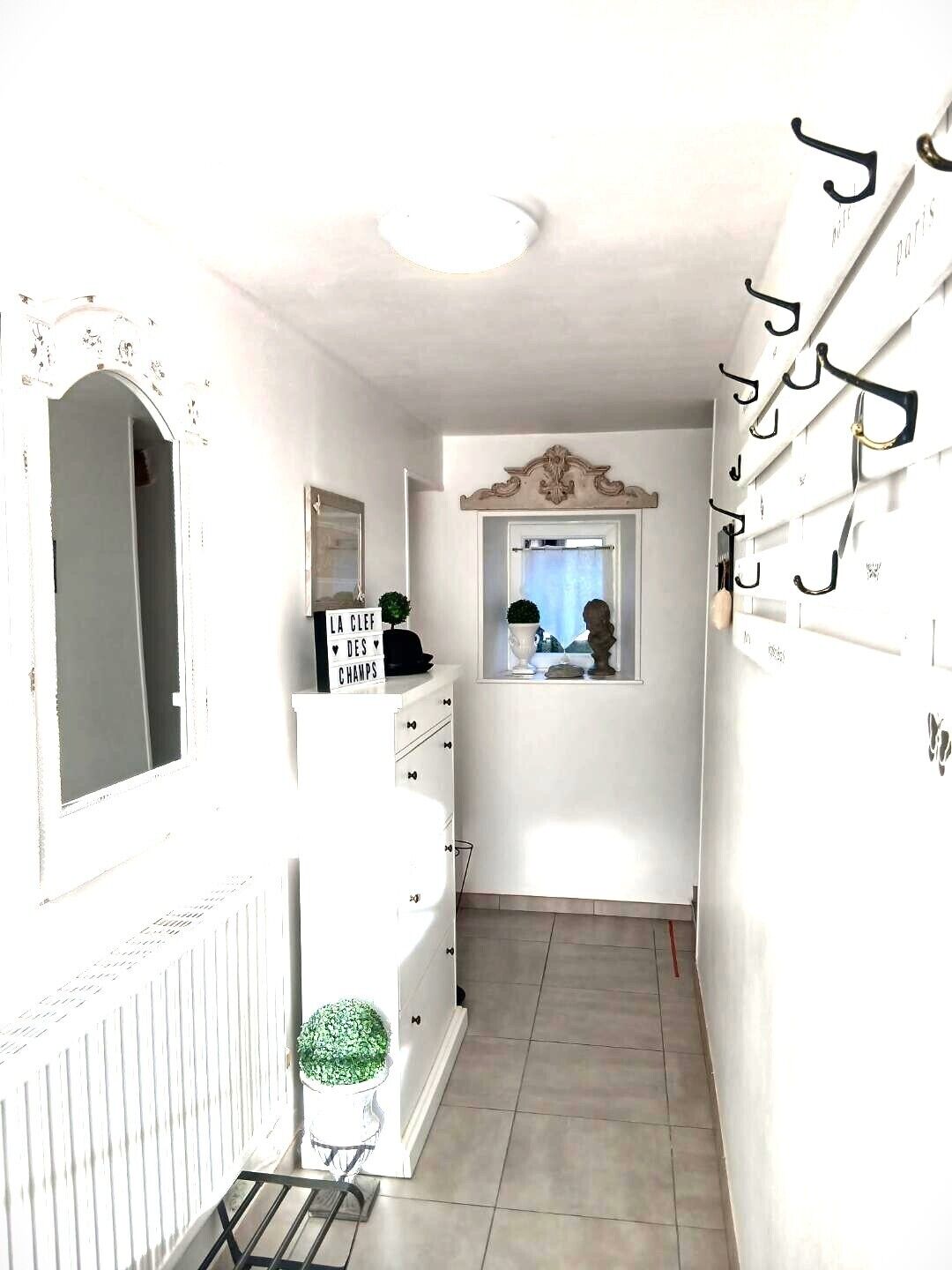 Un pasillo estrecho con un radiador blanco, un espejo, un cartel que dice 'LA CLEF DES CHAMPS' y una ventana con vistas.