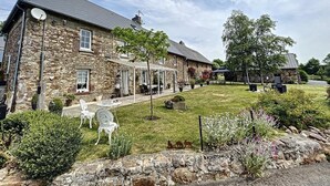 Un edificio de piedra con un patio, mobiliario exterior y un césped bien cuidado.