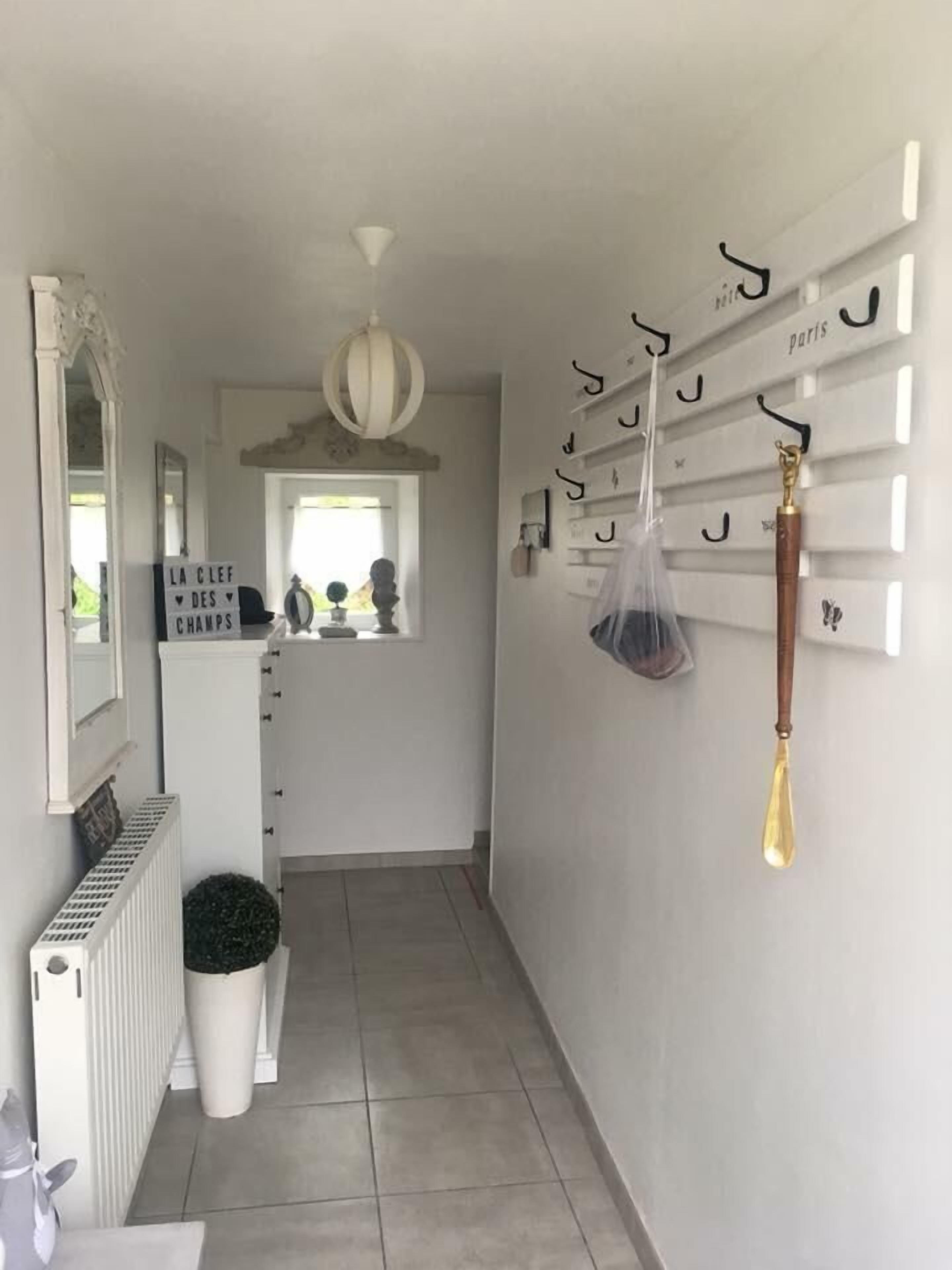 Een gang met een radiator, een bloempot, een spiegel en een kapstok met diverse spullen.