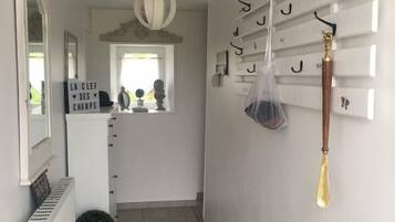 Een gang met een radiator, een bloempot, een spiegel en een kapstok met diverse spullen.
