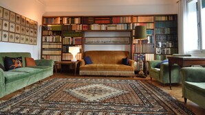 Un salón de biblioteca acogedor, con una estantería grande, un sofá verde y una alfombra estampada.