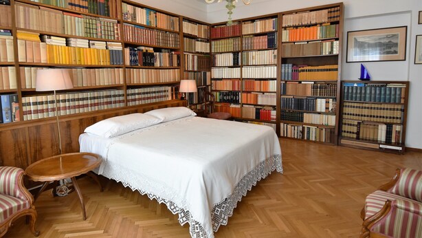 Una sala de biblioteca con una cama grande, estanterías de madera y un candelabro.