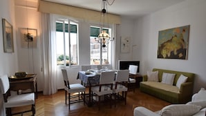Un área de comedor con una mesa dispuesta para cuatro personas, rodeada de sillas, un sofá y un televisor.