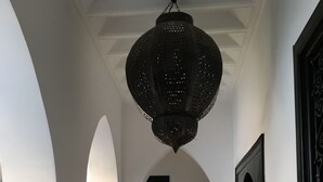 Un couloir aux murs blancs, aux portes noires et orné d’une lanterne suspendue.