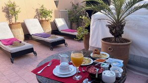 Une table à manger avec des aliments pour le petit-déjeuner, une chaise longue et des plantes en pot dans un espace patio.