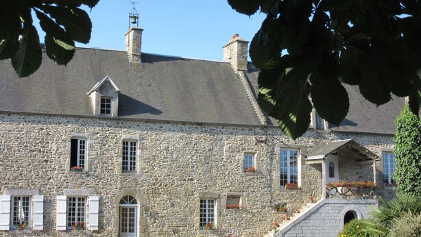Un bâtiment en pierre doté de nombreuses fenêtres, d’une porte et d’un petit escalier menant à un porche.