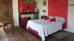 Une chambre à coucher avec un lit, un bureau en bois, une chaise, une cheminée et un mur d’accent rouge.