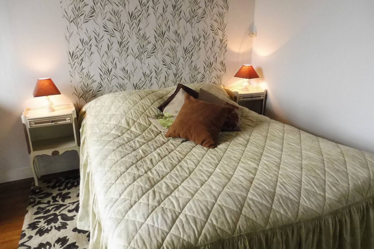 Un lit bien fait, recouvert d’une courtepointe matelassée, avec deux lampes de chevet et un papier peint à motifs.