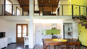 A spacious loft apartment with a high ceiling, a dining area with a wooden table and chairs, a kitchen with light-colored cabinets, and a staircase leading to an upper level. - Lovely apartment in villa for 5 people with WIFI, A/C, pool, TV and patio (Larciano)