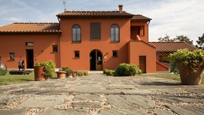 A building with a tiled roof, a central entrance with a door, and multiple windows. There are potted plants and a paved walkway in front. - Lovely apartment in villa for 5 people with WIFI, A/C, pool, TV and patio (Larciano)