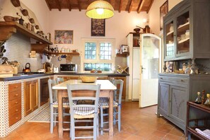 Una cocina con armarios de madera, una mesa de comedor con sillas, una lámpara colgante y una ventana con vistas a árboles.