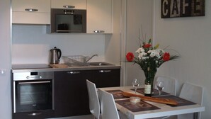A modern kitchen with a built-in oven, a sink, and a dining area with a table set for two. - 2 bedroom, Overlooking Parc Exflora + Sea views. Pool+Beach 200m + Parking + A/C (Antibes)