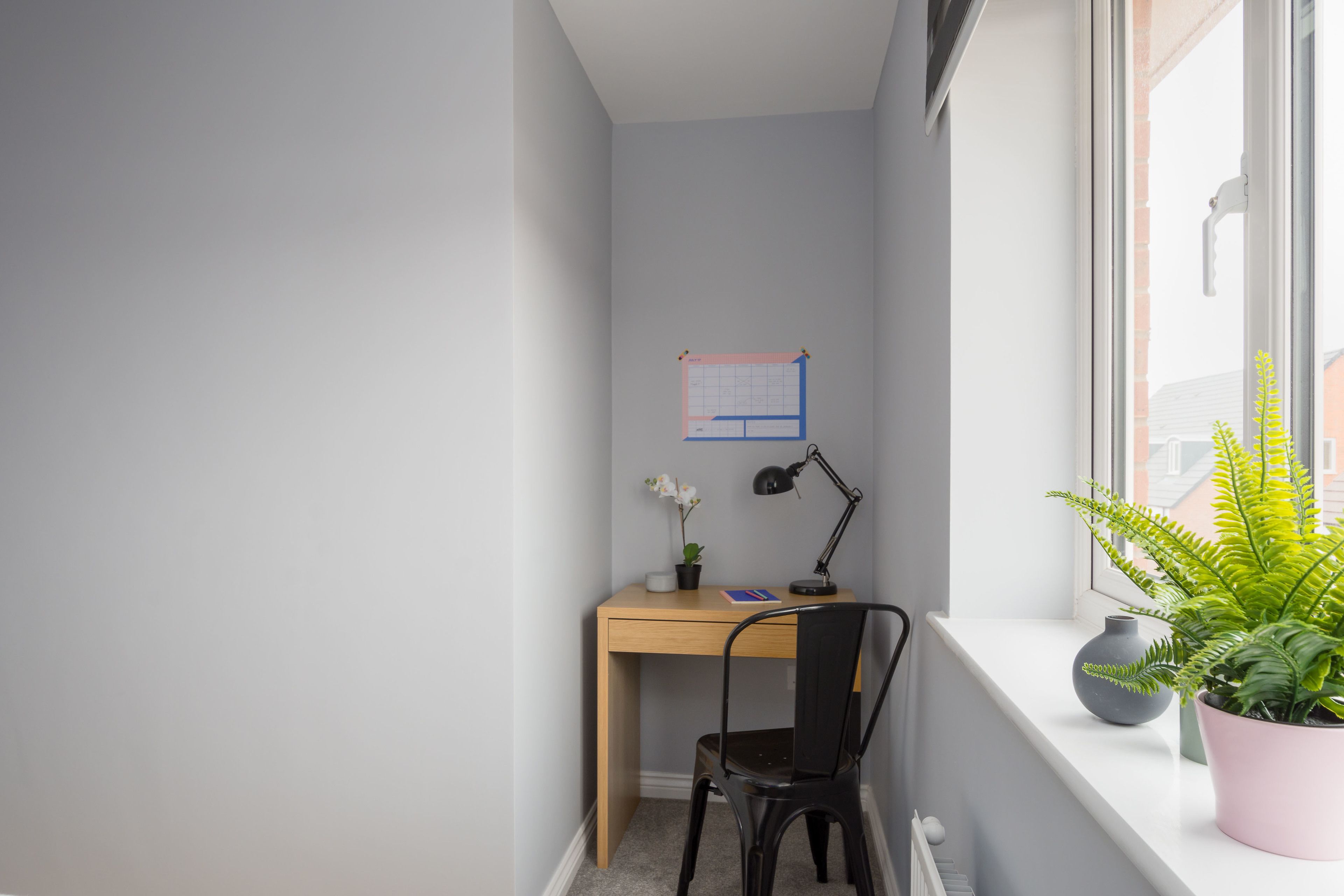 A corner room with a desk, chair, potted plant, and a window with a view.