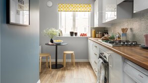 A modern kitchen with white cabinets, a wooden countertop, a Bosch dishwasher, and a window with yellow patterned valance. - Deco Spacious Townhouse (Coventry)