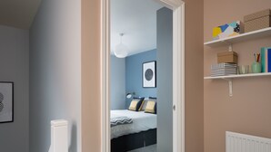 A bedroom with a bed, a bedside table, a shelf with books and decorative items, and a framed picture on the wall. - Deco Spacious Townhouse (Coventry)
