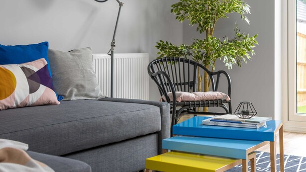 A modern living room with a grey sofa, colorful pillows, a black chair, a small table with books, a floor lamp, and a potted plant. - Deco Spacious Townhouse (Coventry)