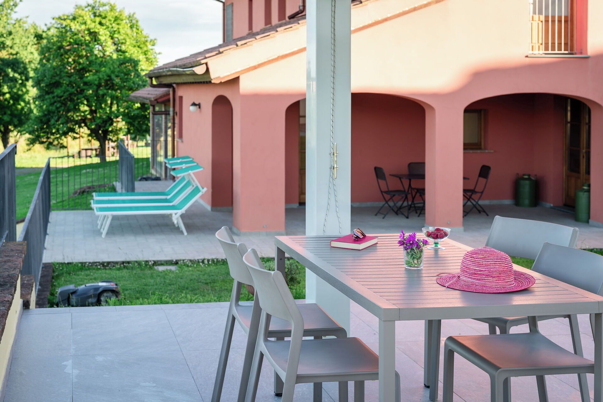 A patio with a table, chairs, and a bench. There are outdoor chairs and a table with a hat and flowers.