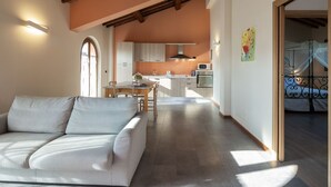 Un saló modern amb un sofà, una zona de menjador i una cuina amb armaris de fusta i un microones.