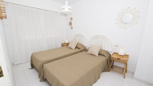 A bedroom with two beds, a nightstand with a lamp, a mirror, and a window with curtains. - A94 APOLO 7 ESC 6 3º 14 (Calpe)