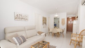 A living room with a sofa, a glass coffee table, a dining table with chairs, and a kitchen area with a refrigerator. - A94 APOLO 7 ESC 6 3º 14 (Calpe)