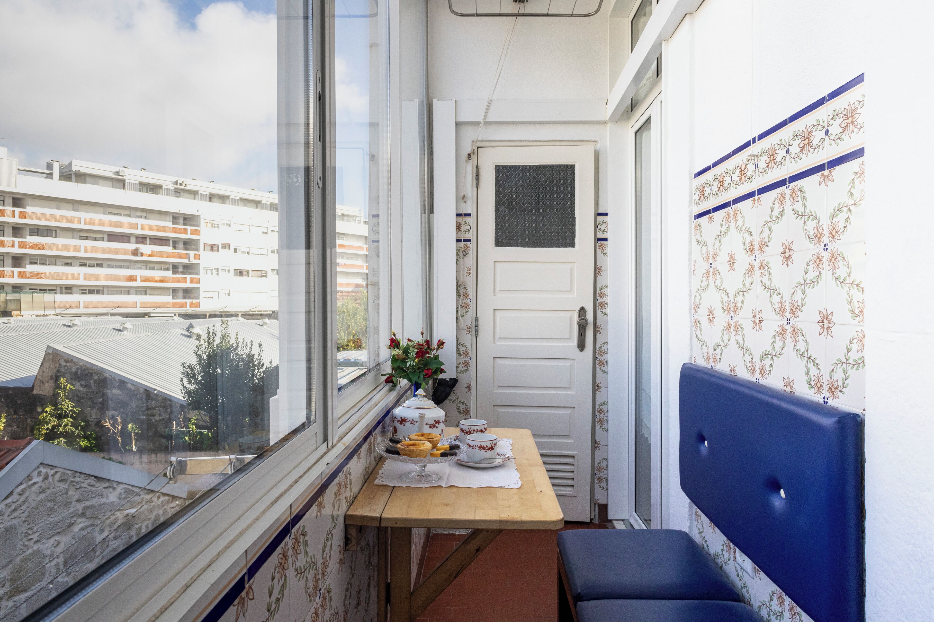Un balcon avec une table dressée pour le petit-déjeuner, une porte et une vue sur les bâtiments.