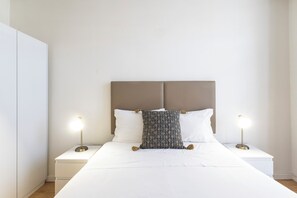 A neatly made bed with a patterned pillow, two bedside lamps, and a white wardrobe.