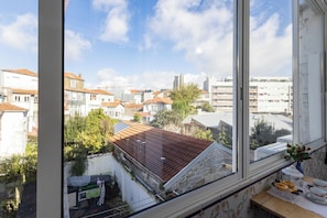 A view from a window overlooking a cityscape with buildings, a clear sky, and a table with items on it.