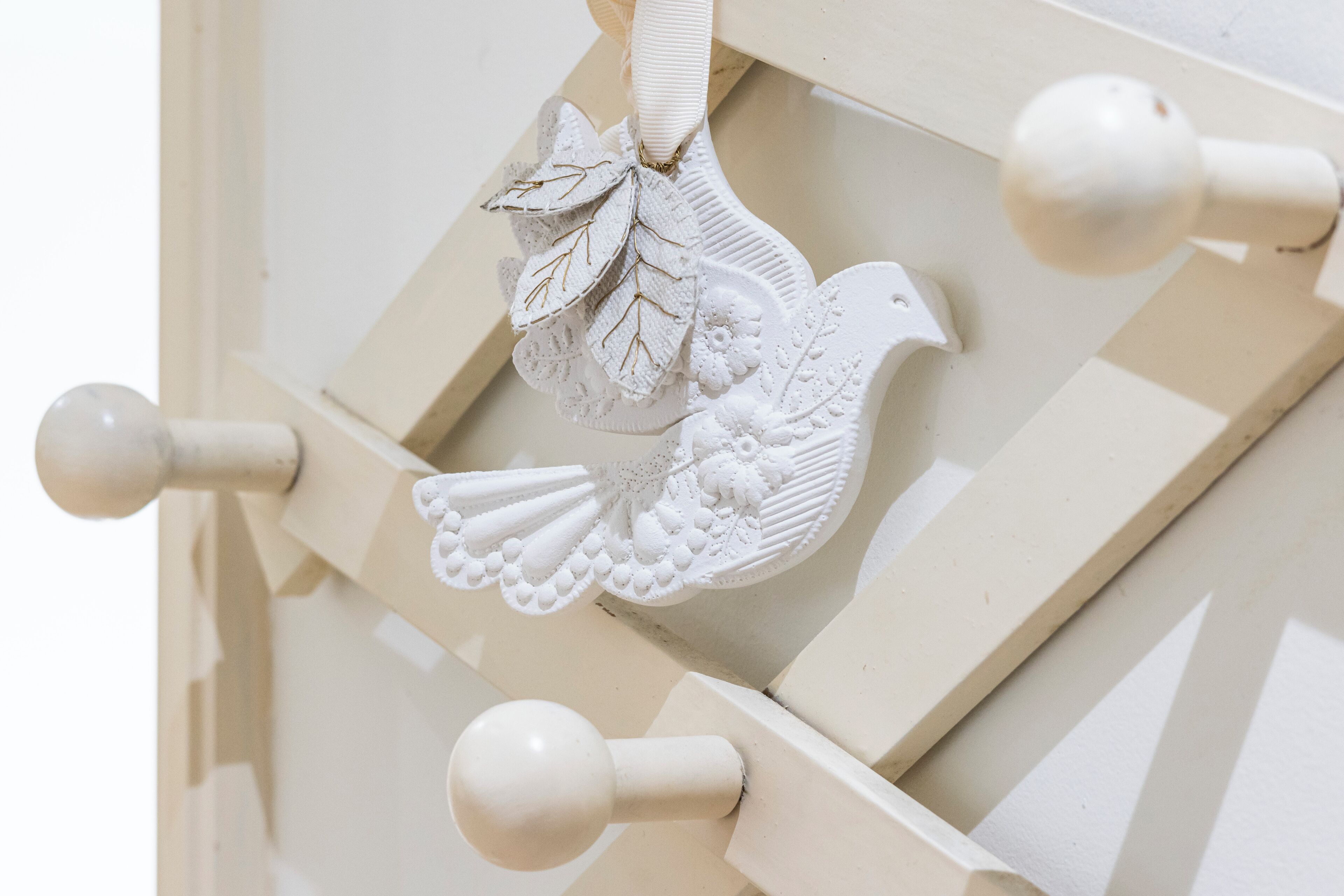 Un pájaro decorativo blanco con un lazo, sobre una pared beige con un diseño geométrico.