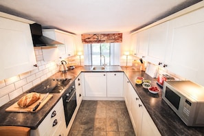 A compact kitchen with white cabinets, a black countertop, a stove, a sink, and a microwave. - Kirkstone Cottage, ideal for romantic break, close to Ambleside town centre and pubs (Ambleside)
